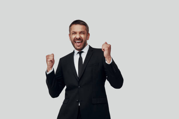 istock Charming young man in full suit cheering while standing against grey background 1184378438