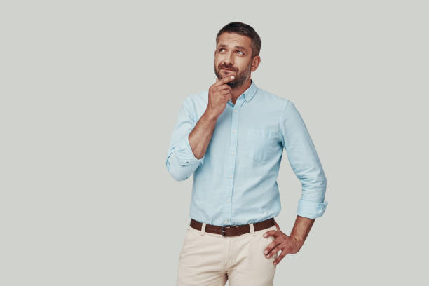 istock Handsome young man looking away and keeping hand on chin while standing against grey background 1184380000