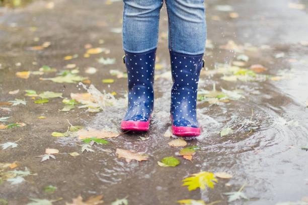 istock Woman in blue rubber boots jumping in puddle 1184380029