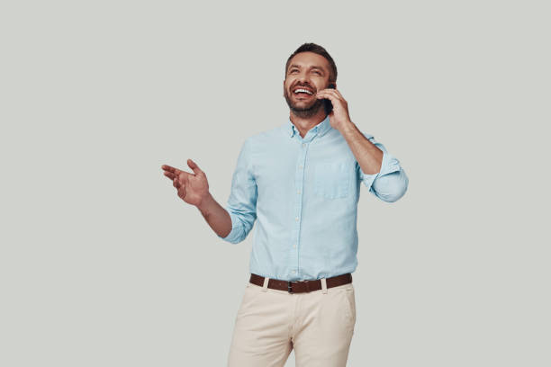 istock Handsome young man talking on the phone and smiling while standing against grey background 1184380226