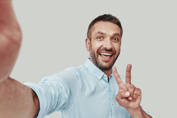 istock Self portrait of handsome young man looking at camera and smiling while standing against grey background 1184380358