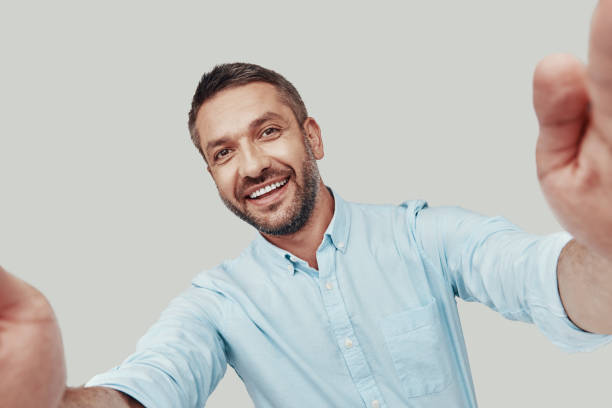 istock Self portrait of handsome young man looking at camera and smiling while standing against grey background 1184380427