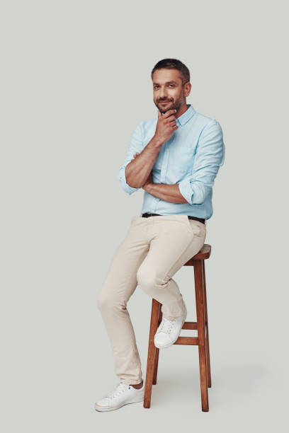 istock Handsome young man looking at camera and smiling while sitting against grey background 1184381150
