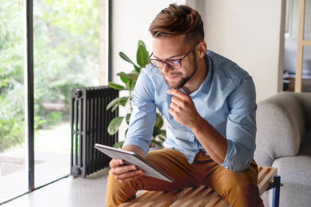 молодой человек смотрит на цифровой планшет - relaxation indoors reading one person стоковые фото и изображения