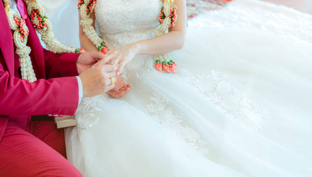 istock Groom put wedding diamond ring on bride finger for proposal on wedding ceremony day. Bride and groom in white wedding dress and red suit and wedding garlands. Marriage or matrimony. Begin couple life. 1184385228