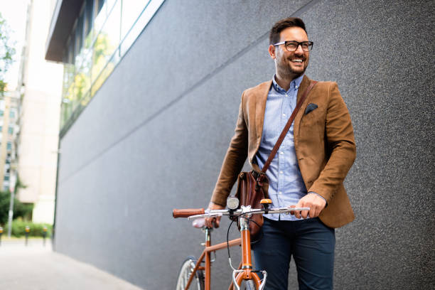 glücklicher junger stylischer geschäftsmann geht mit dem fahrrad zur arbeit - urban man stock-fotos und bilder