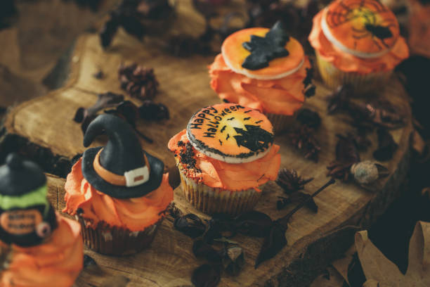 Delicious Halloween cupcakes Side view of cupcakes with orange cream and Halloween decoration on top arranged on wood log. halloween cupcake stock pictures, royalty-free photos & images
