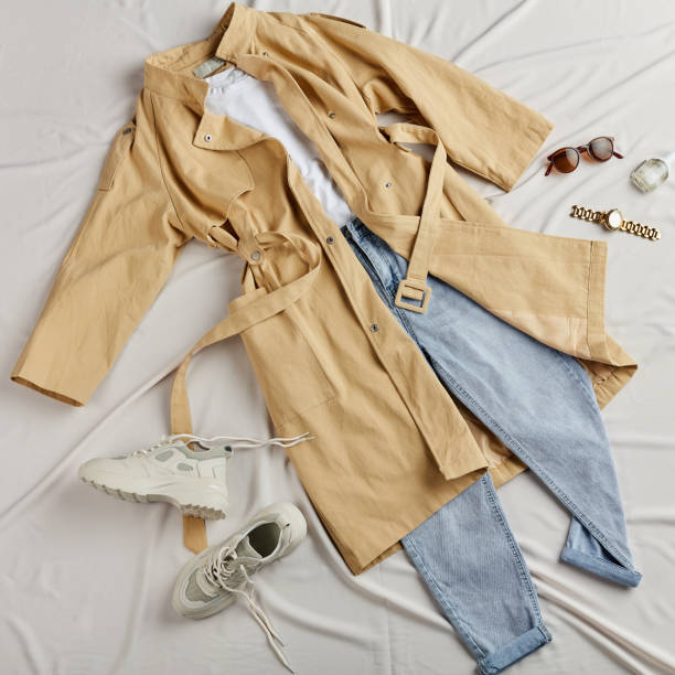 istock modern beige coat, jeans and white trainers lying on the white sheet 1184393434