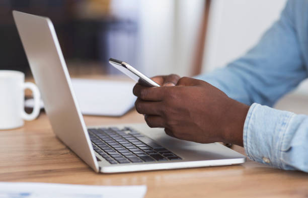 istock Black man typing message on smartphone and working with laptop 1184393733