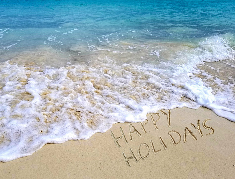 happy holidays text on tropical beach with ocean surf