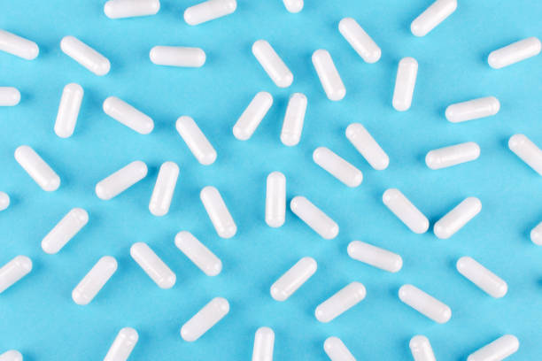 파란색 배경에 흰색 의학 캡슐, 위에서보기 - capsule pill white nutritional supplement 뉴스 사진 이미지