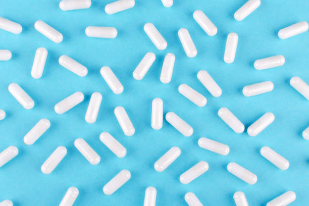 cápsulas de medicina branca em fundo azul, vista de cima - capsule pill white nutritional supplement - fotografias e filmes do acervo