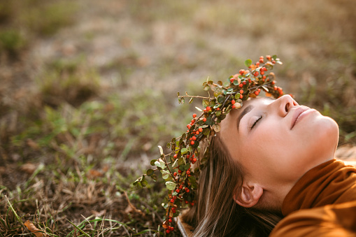 Pretty blonde smile woman with flower wreath lying down in grass enjoys sunset at picnic