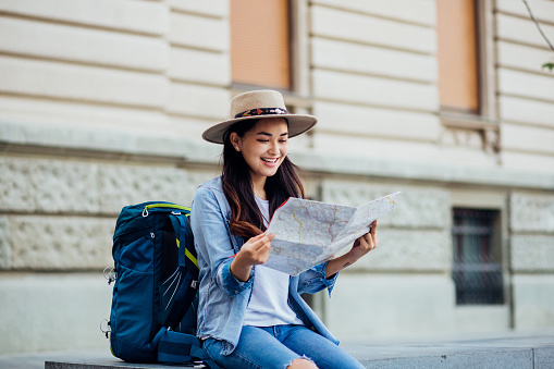 Young woman with a backpack traveling alone and exploring the city map.