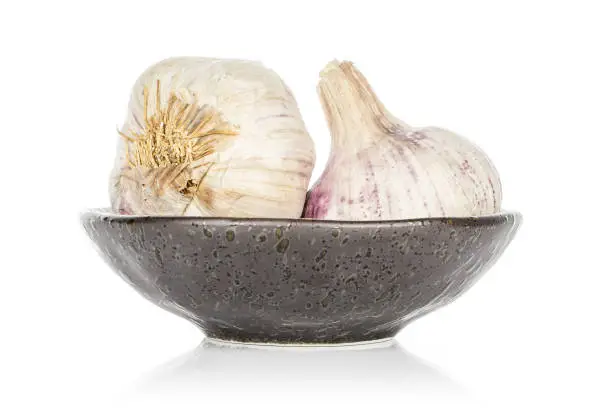 Group of two whole aromatic white garlic on glazed bowl isolated on white background