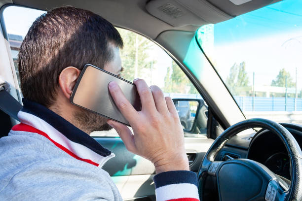 um homem que prende um telefone móvel de prata perto de sua orelha e que fala nele ao conduzir. perigo de usar o telefone em um carro - driving mobile phone car talking - fotografias e filmes do acervo