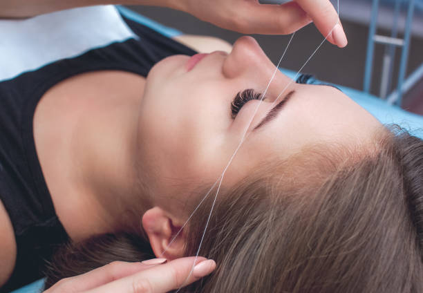 der make-up-künstler zupft augenbrauen mit einem faden nah. professionelles make-up und gesichtspflege im schönheitssalon - removing tweezing eyebrows eyebrow caucasian stock-fotos und bilder