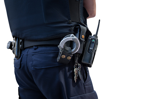 Cropped view of a police officer's waist. He is wearing his equipment belt with gun holster, handcuffs, radio and other gear. He is an Hispanic mid adult man in his 30s standing outdoors.