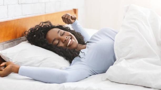 happy african young woman stretching in bed - wake up stretching women black imagens e fotografias de stock