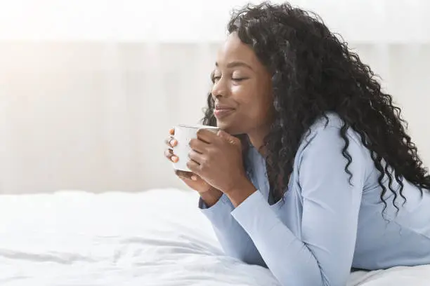 Photo of Joyful girl relaxing in bed with cup of coffee