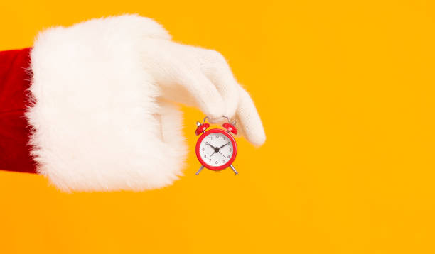 istock Santa hand holding small red alarm clock with time on orange 1184412979