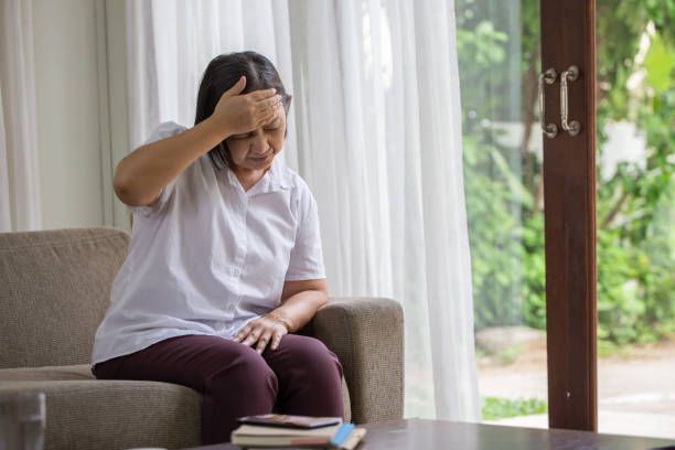 Asian senior woman sitting on sofa having headache at home. old female   stressed dizzy . elderly touching her head with her hands while having migraine or alzheimer .memory loss . indoor. copy space stock photo