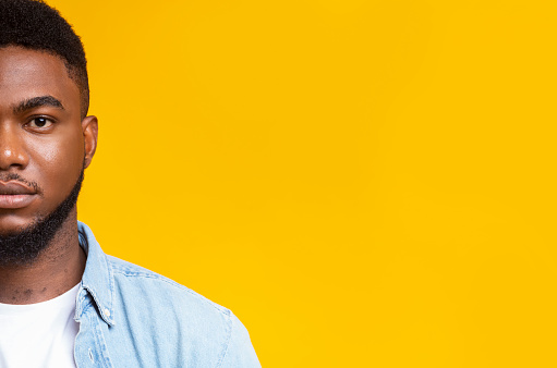 Half face portrait of confident african american man with beard on yellow studio background, free space