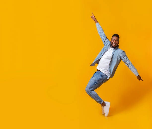 Funny black guy posing on tiptoes over yellow background in studio Funny african american man posing on tiptoes over yellow background in studio tiptoe stock pictures, royalty-free photos & images