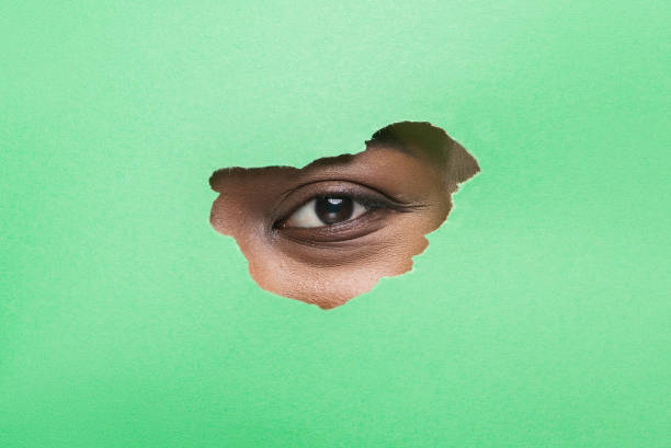 istock Black Woman's Eye Without Mascara Looking Through Torn Green Paper 1184417397