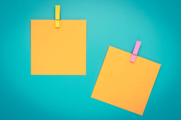 Yellow sticky note with clothespin. Two orange stickers on a blue bulletin board. Reminder, planning concept. Turquoise background. stock photo