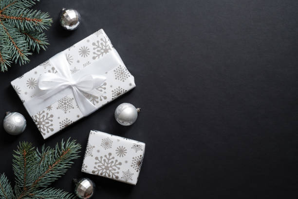 istock Gift boxes wrapped silver paper and fir tree branches with decorative balls over black background. Christmas banner mockup, New year postcard template. Flat lay, top view, overhead 1184418686