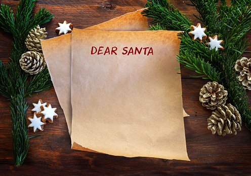 Paper sheet with text Dear Santa, between fir branches, cinnamon stars and pine cones on rustic dark wood, Christmas wish list or letter to Santa Claus with copy space, top view from above