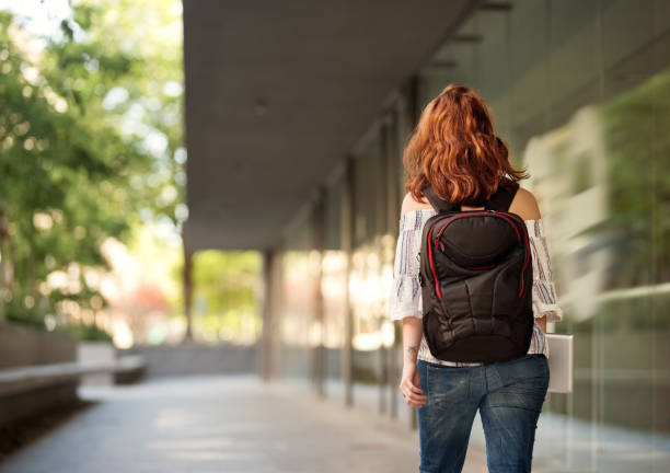 She never miss any class Rear view shot of a young female university student with backpack walking down a paved road never stock pictures, royalty-free photos & images