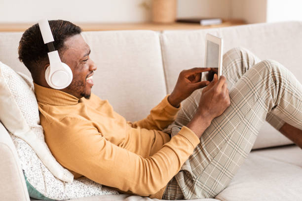 istock Man In Headphones Using Tablet Relaxing On Sofa At Home 1184422568