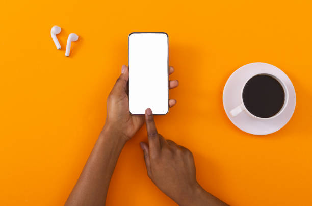 istock Female hands touching cellphone with blank screen on orange background 1184423456