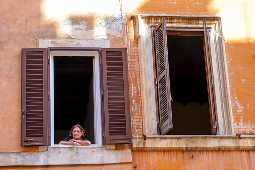 Rome, Italy, October 21 - An elderly lady looks out of the large windows of her house in a street of Rione Monti, in the heart of Rome, a district included in the area between the Basilica of Santa Maria Maggiore and the Roman Forum. Photo in HD format
