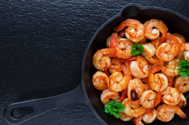 tasty roasted shrimps in a cast iron pan with parsley and garlic, on black background - shrimp pan cooking prepared shrimp imagens e fotografias de stock