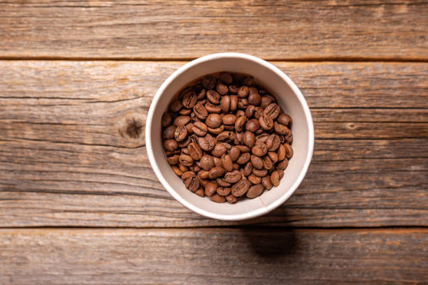 istock Coffee grains in a paper cup on wooden background. 1184425084