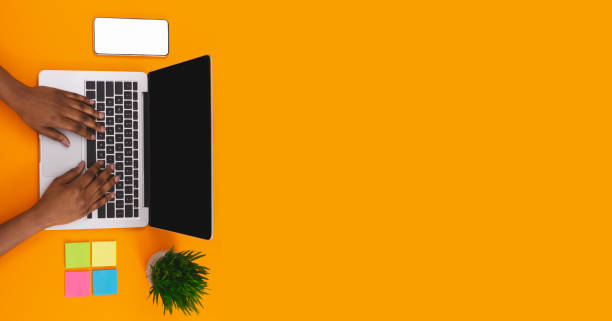 donna nera che digita su laptop su worplace su sfondo arancione - human hand computer equipment household equipment foto e immagini stock