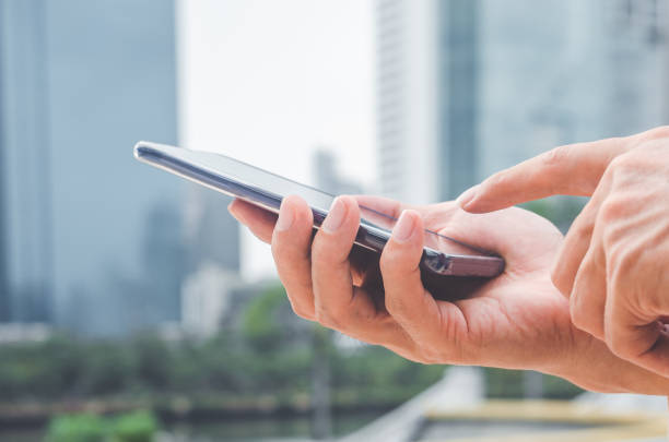 istock close up handsome man using hand typing smartphones and touch screen working search with app devices outdoor in city with sunrise and building background. 5G technology connecting the world. 1184426693