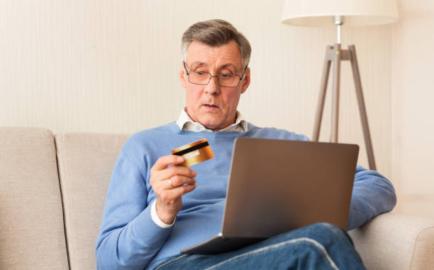 istock Senior Man Using Credit Card And Laptop Sitting On Sofa 1184426923