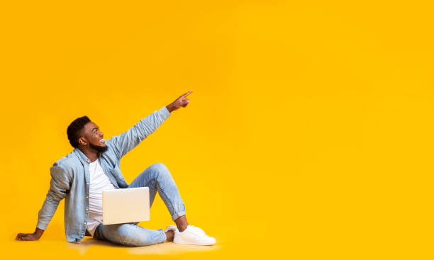 istock African man sitting with laptop and pointing at copy space 1184426948