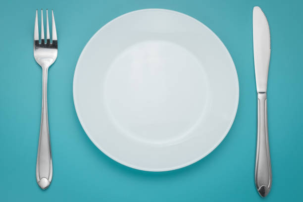 istock White empty plate with fork and knife on blue background. Turquoise backdrop. Laying, table appointments. 1184435342