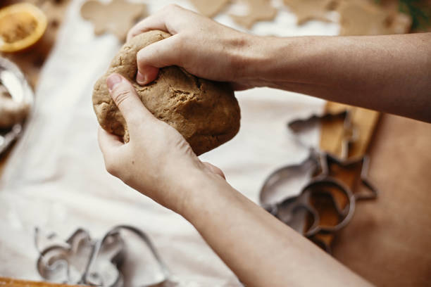 istock Making christmas gingerbread cookies. Hands kneading raw dough on background of rolling pin,metal cutters, anise, ginger, cinnamon, pine cones, fir branches on rustic table. 1184437270