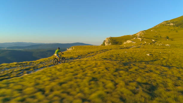 istock AERIAL: Flying above an active man riding his bicycle down the grassy mountain. 1184438423