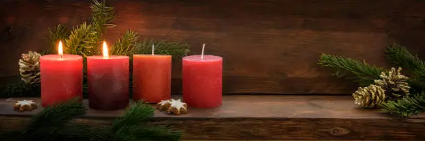 Second Sunday in Advent, four red candles, two of them are burning, fir branches and Christmas decoration on dark rustic wood, wide panoramic format with copy space, selected focus