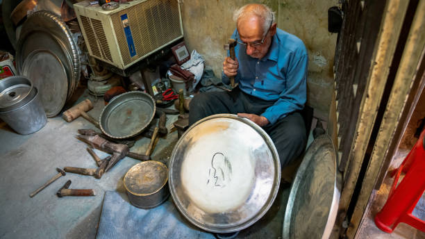Yazd, Iran - May 2019: Old Iranian man working with his hammer in a store with various old tools