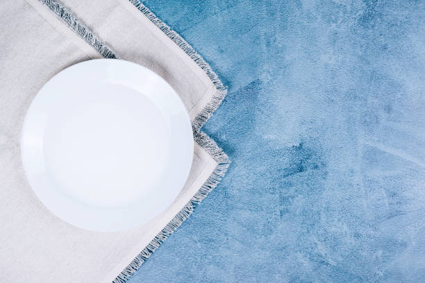 istock Empty circle plate on white linen napkins on blue grey background. 1184450522
