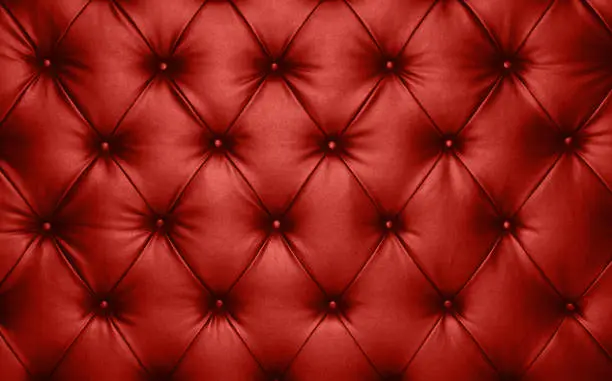 Close up background texture of scarlet red capitone genuine leather, retro Chesterfield style soft tufted furniture upholstery with deep diamond pattern and buttons