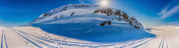Panorama view at Atoklinten Mountain in Lappland, Northern Sweden, side view. All snowmobiles drive here, many trails around. Bright sun shines just above the top, snow, blue skies, much copy space vista panorámica en la montaña atoklinten en lappland, norte de suecia, vista lateral. todas las motos de nieve conducen aquí, muchos senderos alrededor. sol brillante brilla justo por encima de la parte superior, nieve, cielos azules, mucho espacio de